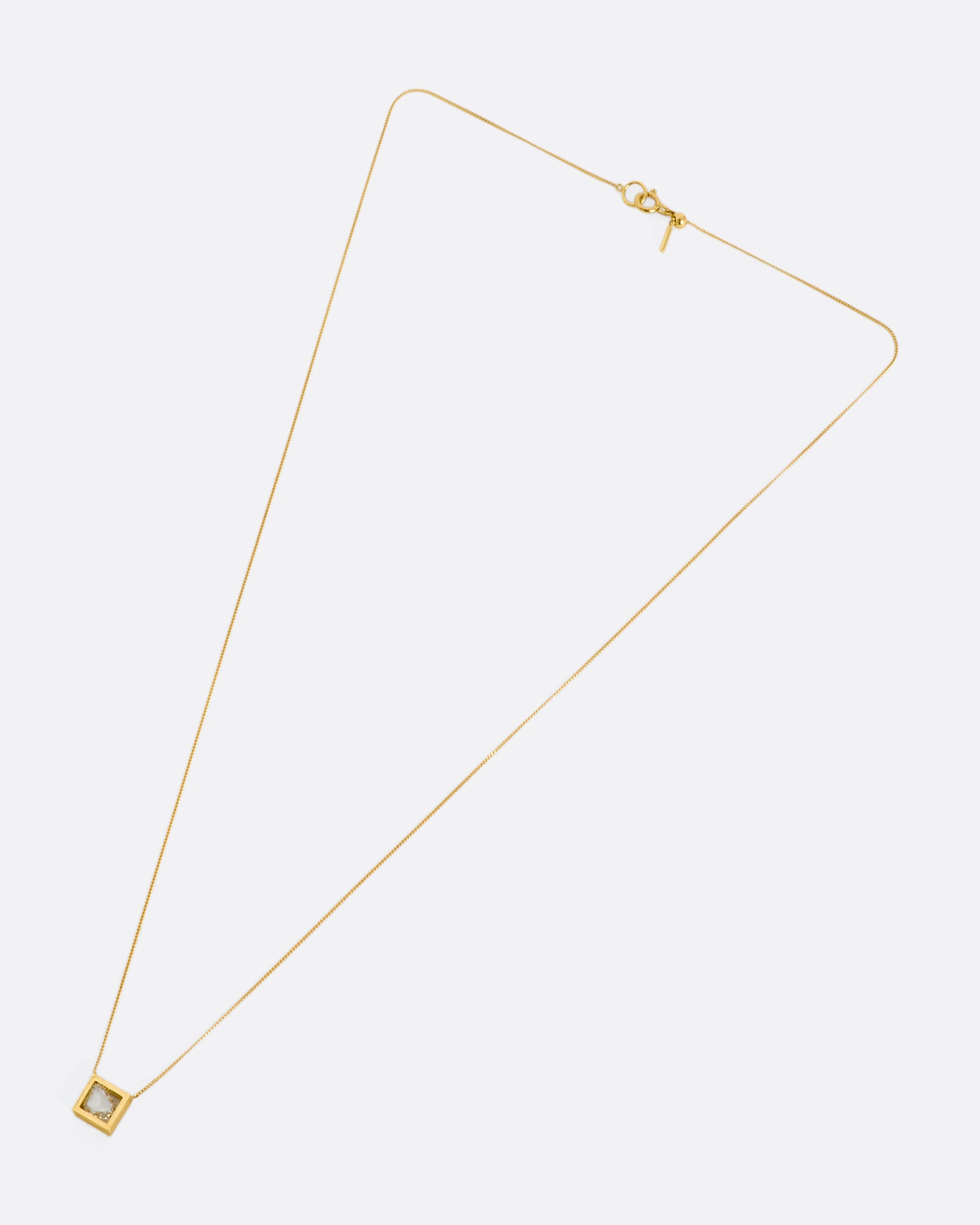 A yellow gold square fixed pendant frame holds a rose cut diamond slice hanging from a chain. View laying flat.