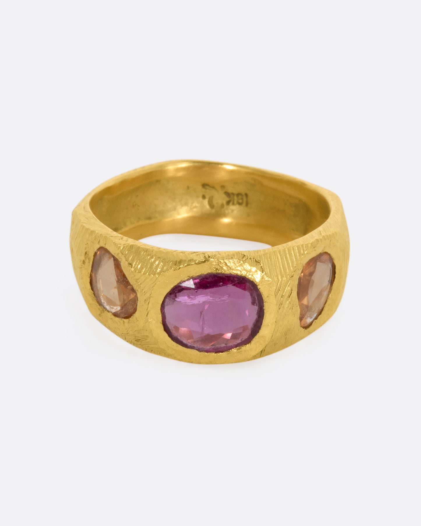 A yellow gold band with three large sapphires, one pink and two orange. Shown from the front.