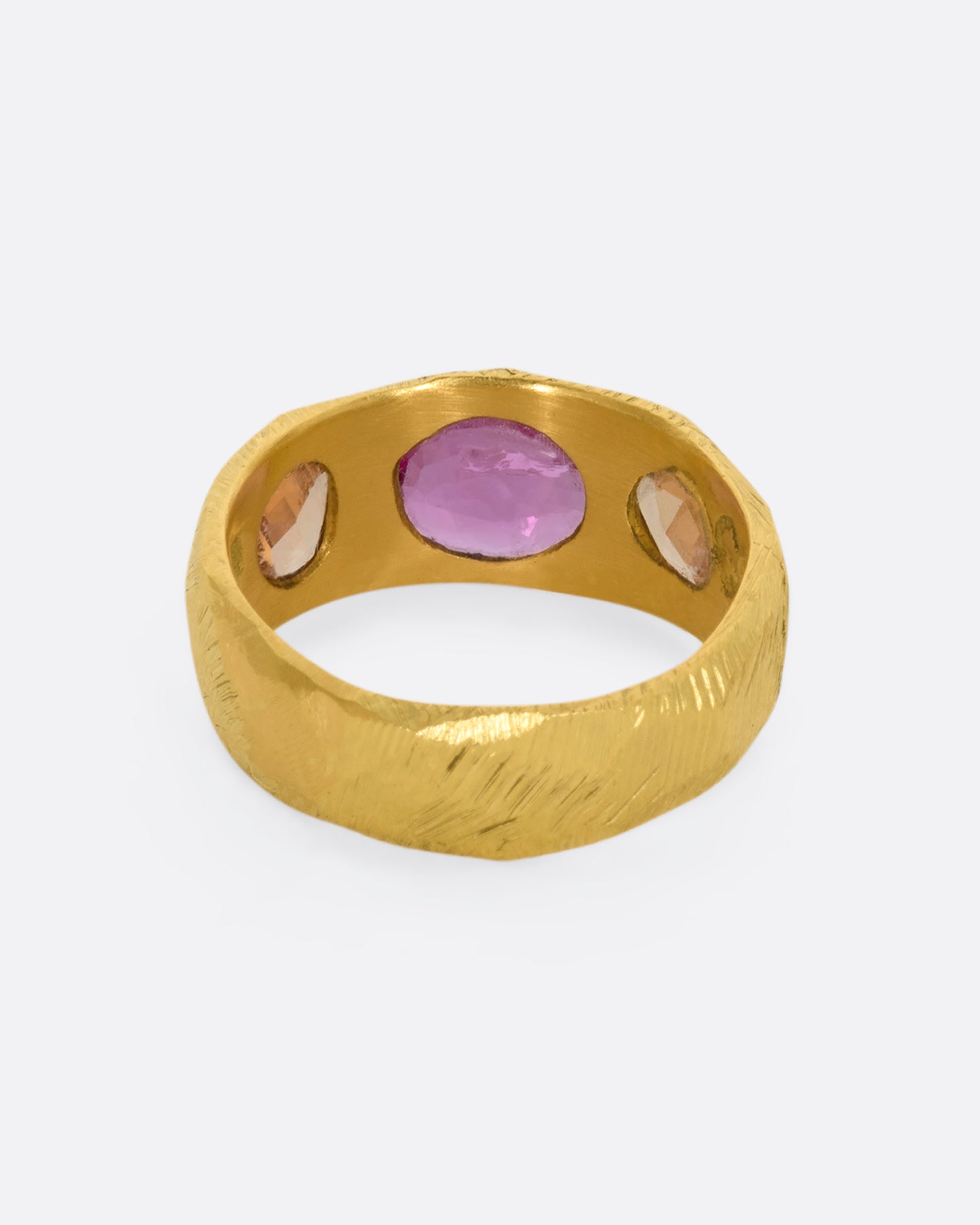 A yellow gold band with three large sapphires, one pink and two orange. Shown from the back.