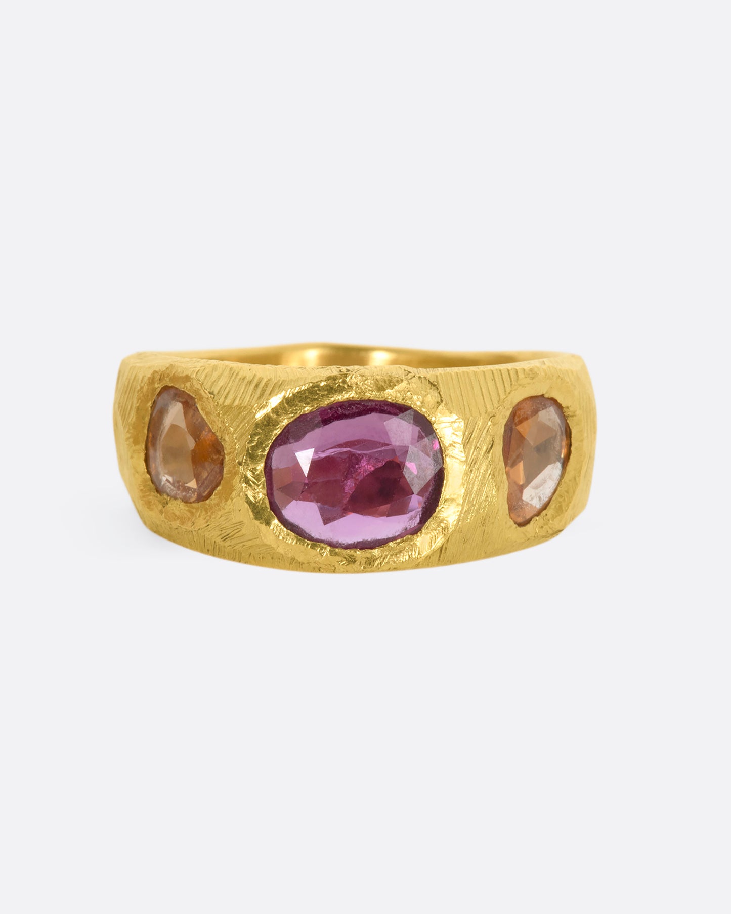 A yellow gold band with three large sapphires, one pink and two orange. Shown from the front.