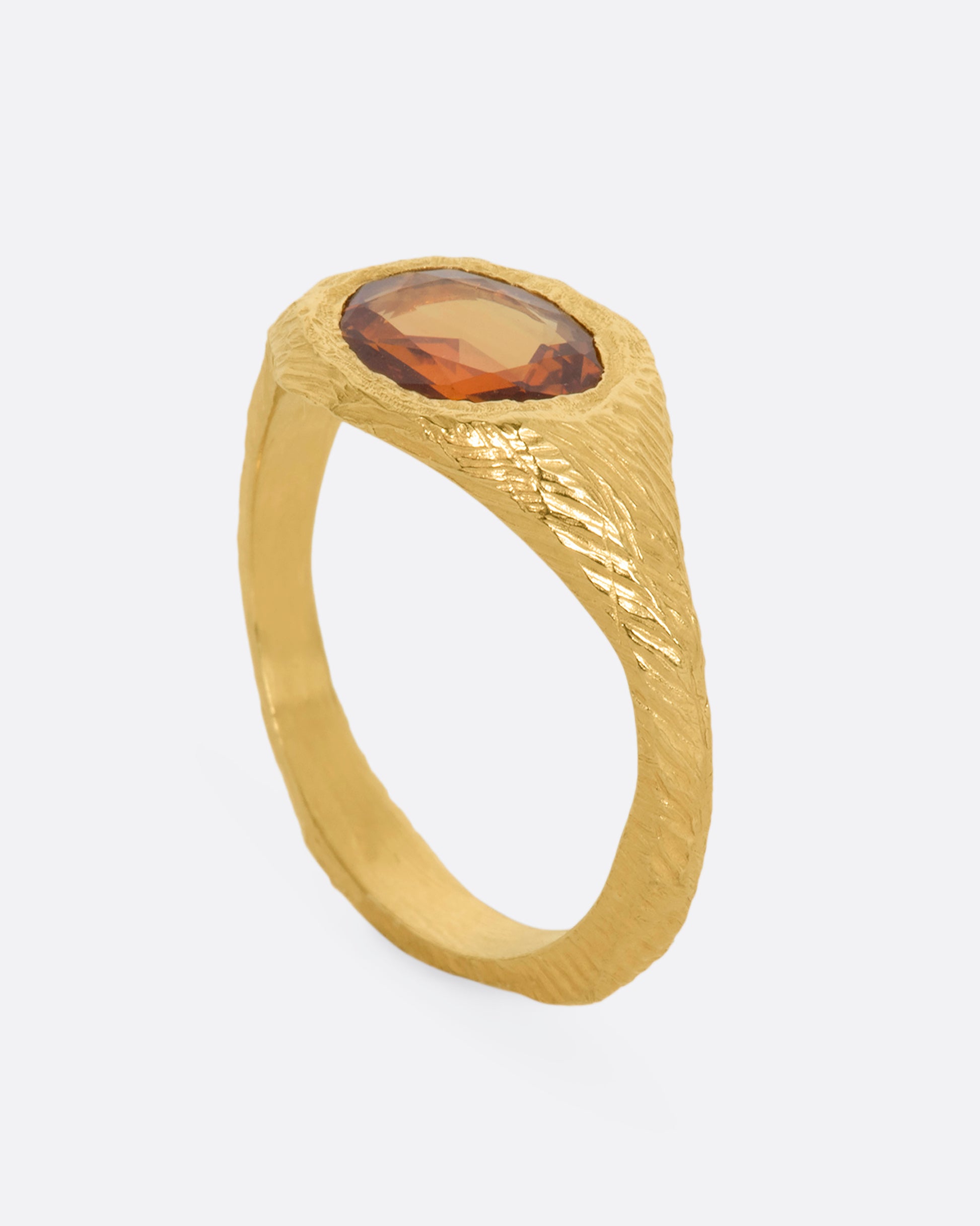 A hand carved yellow gold ring with an orange sapphire. View from the side standing up.