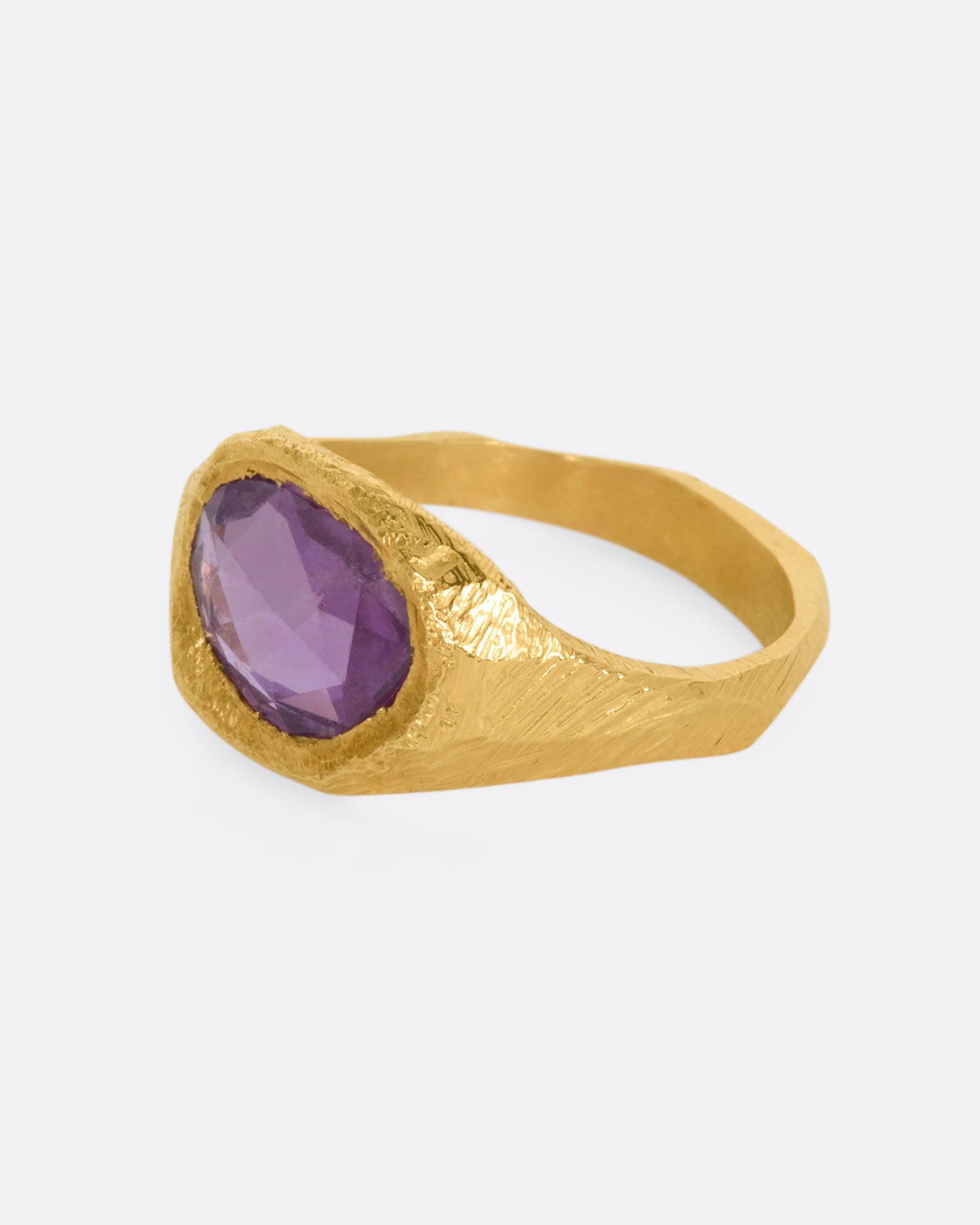 A textured yellow gold signet style ring with a rose cut purple sapphire. View from the side.