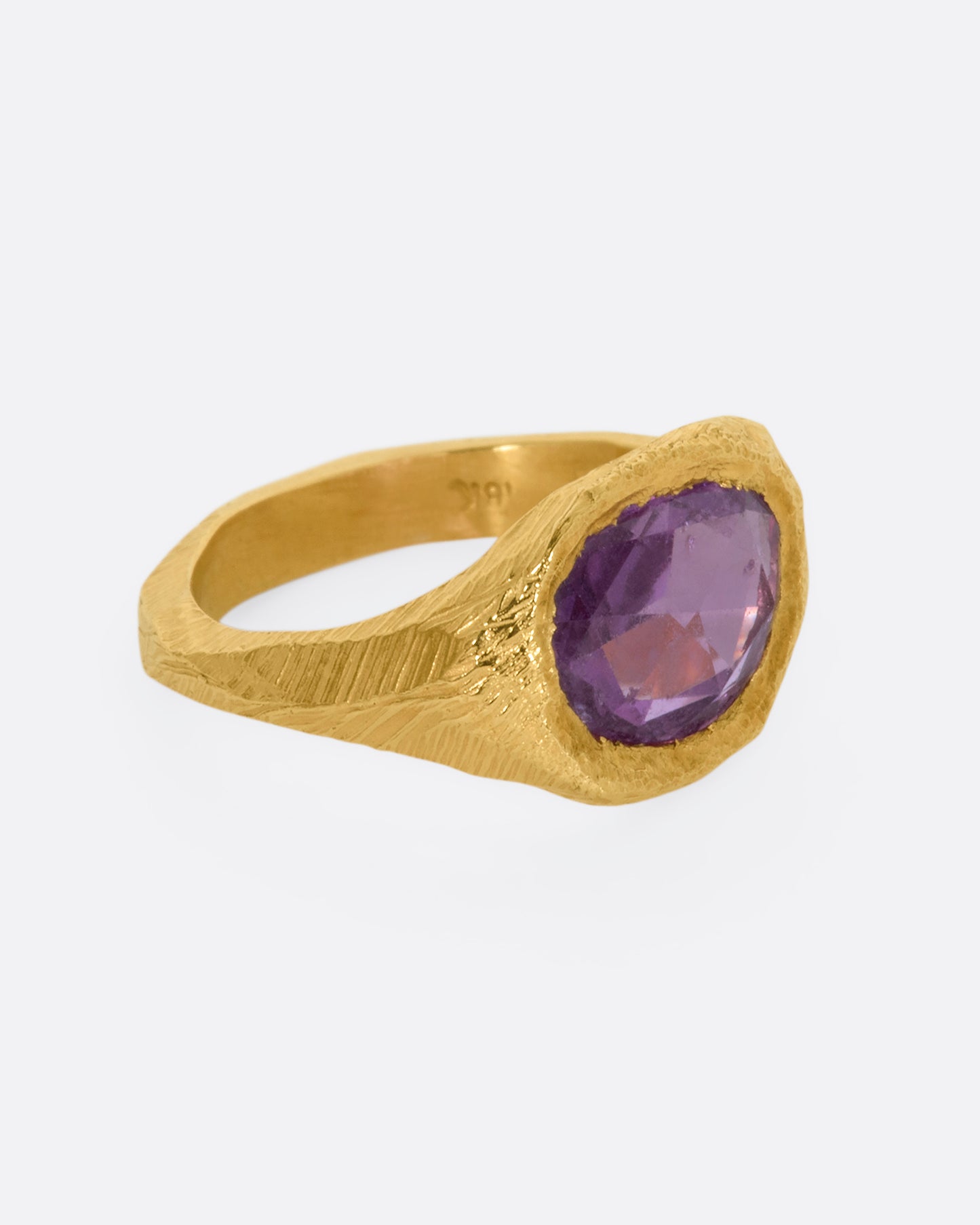 A textured yellow gold signet style ring with a rose cut purple sapphire. View from the alternate side.