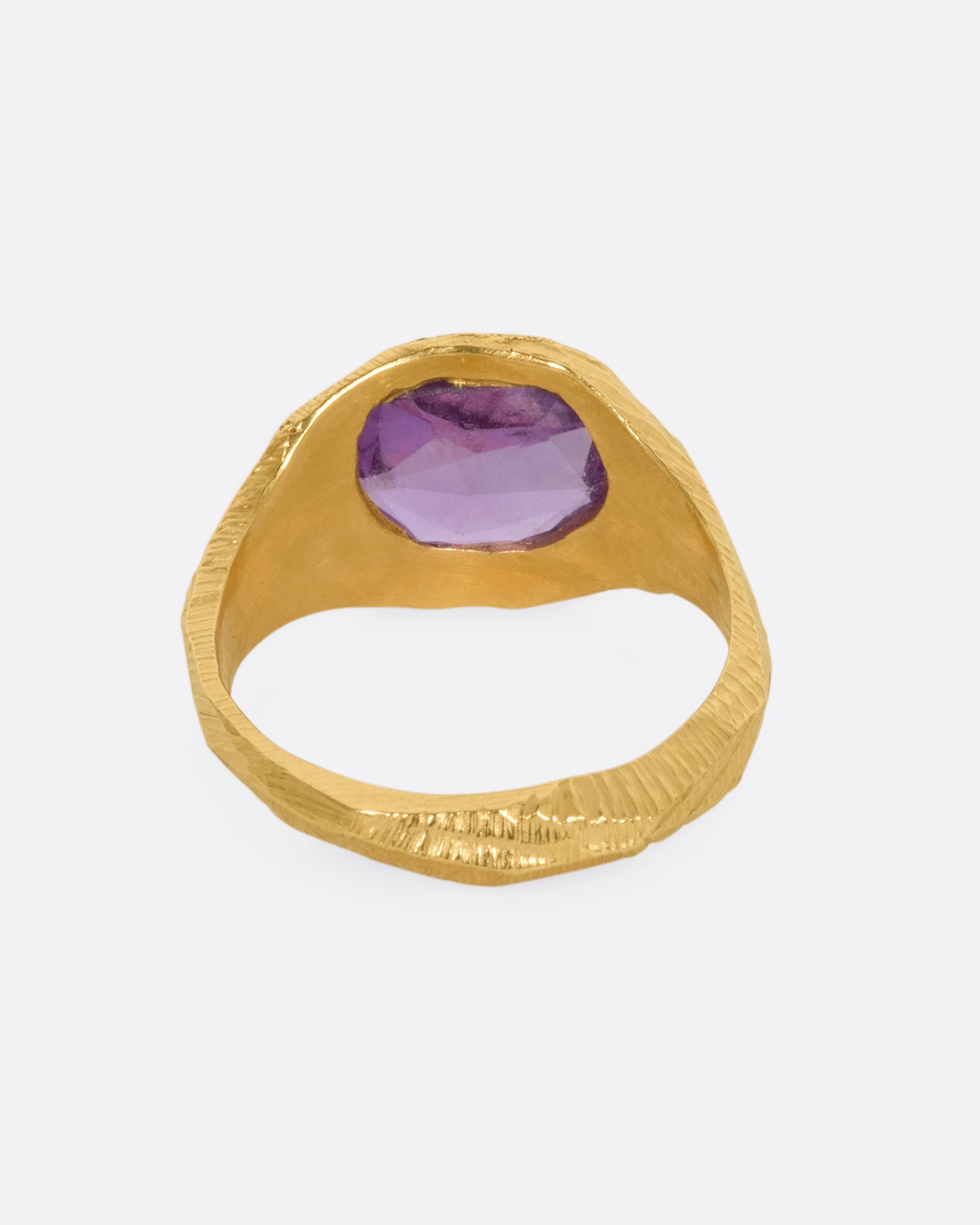 A textured yellow gold signet style ring with a rose cut purple sapphire. View from the back.