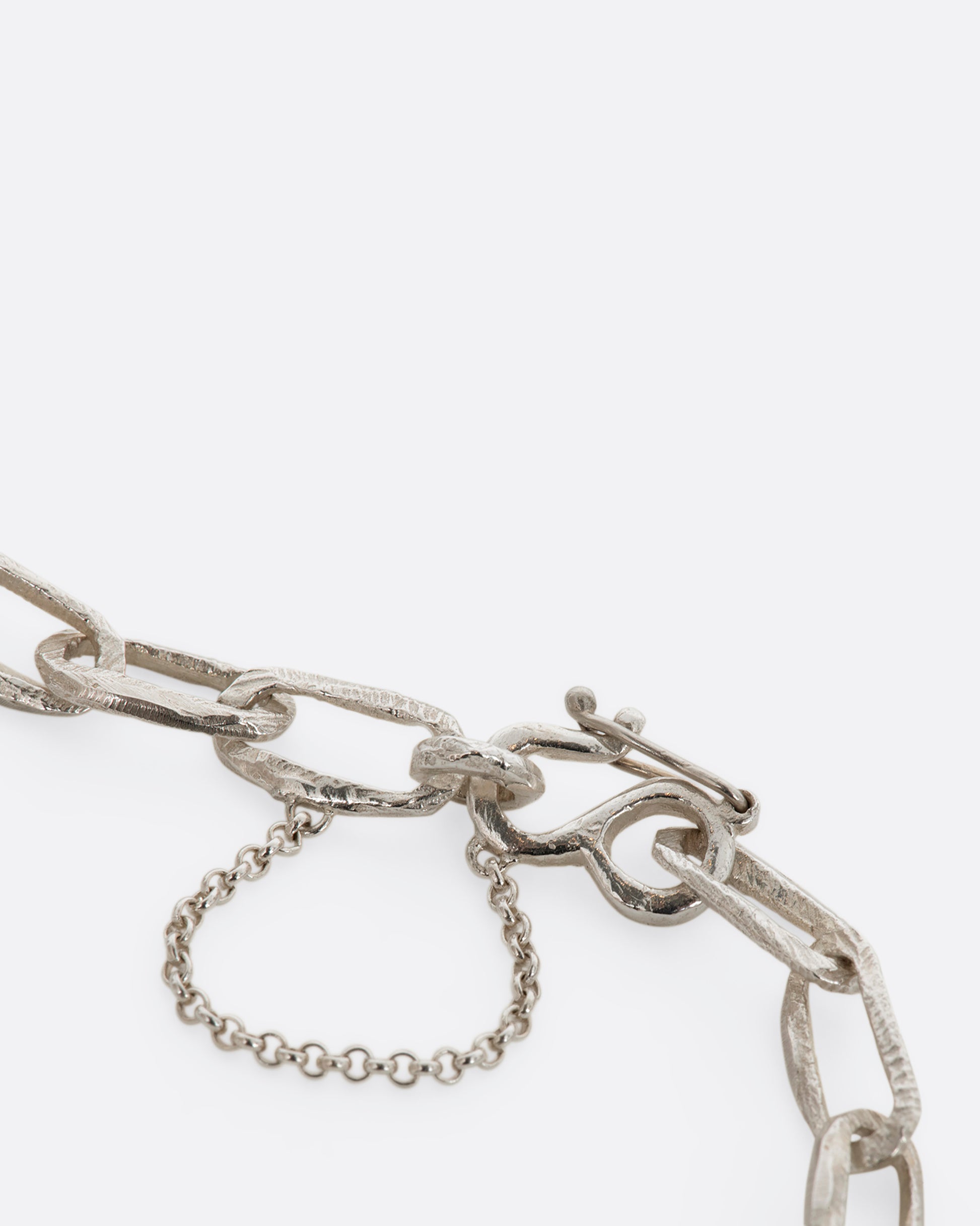 A sterling silver chain link bracelet with textured links and a safety chain. View of the closure close up.