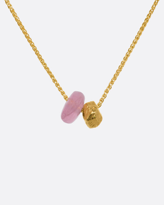 A pink tourmaline bead and gold textured bead hang from a yellow gold chain. View up close of the beads.