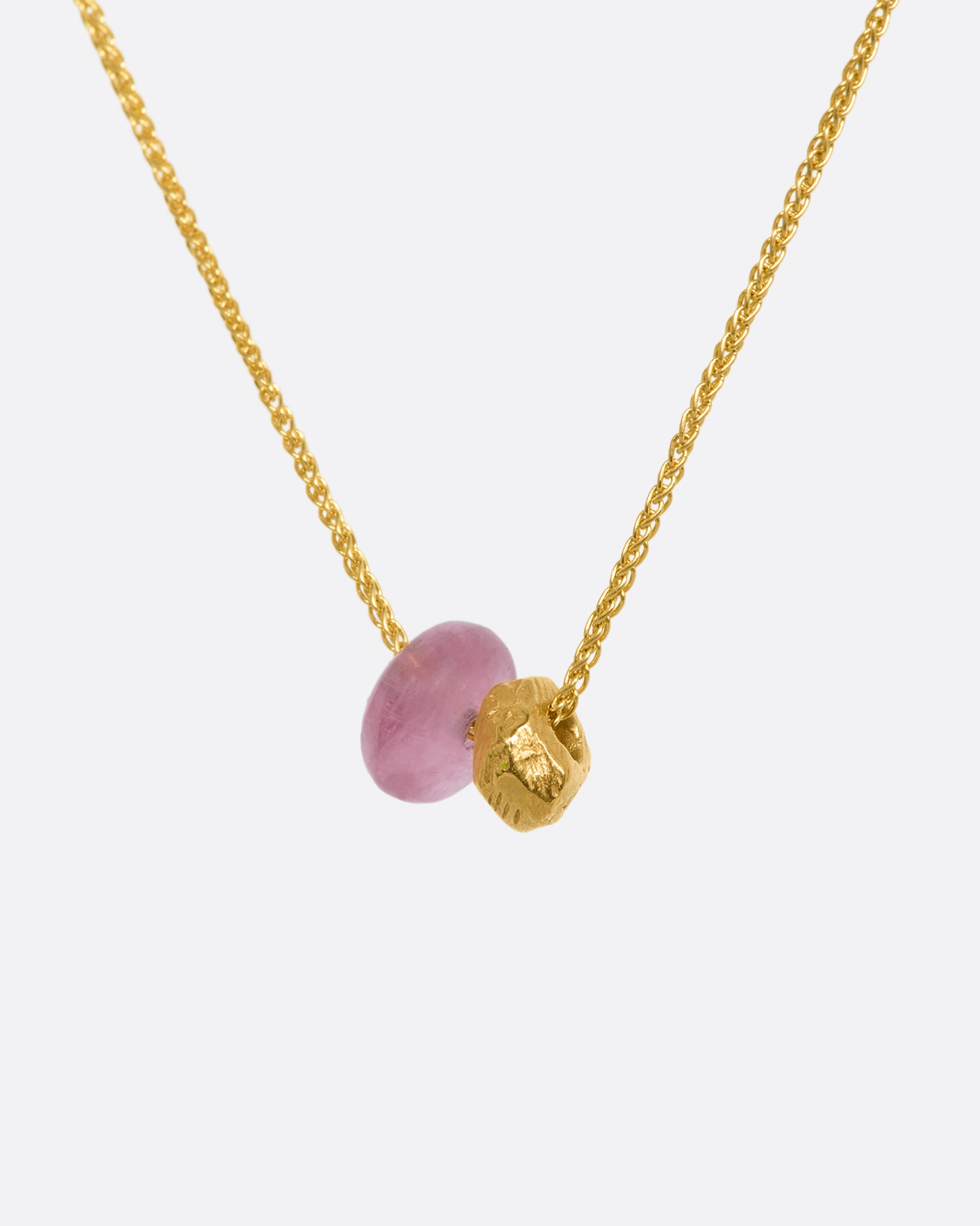 A pink tourmaline bead and gold textured bead hang from a yellow gold chain. View up close of the beads from the side.