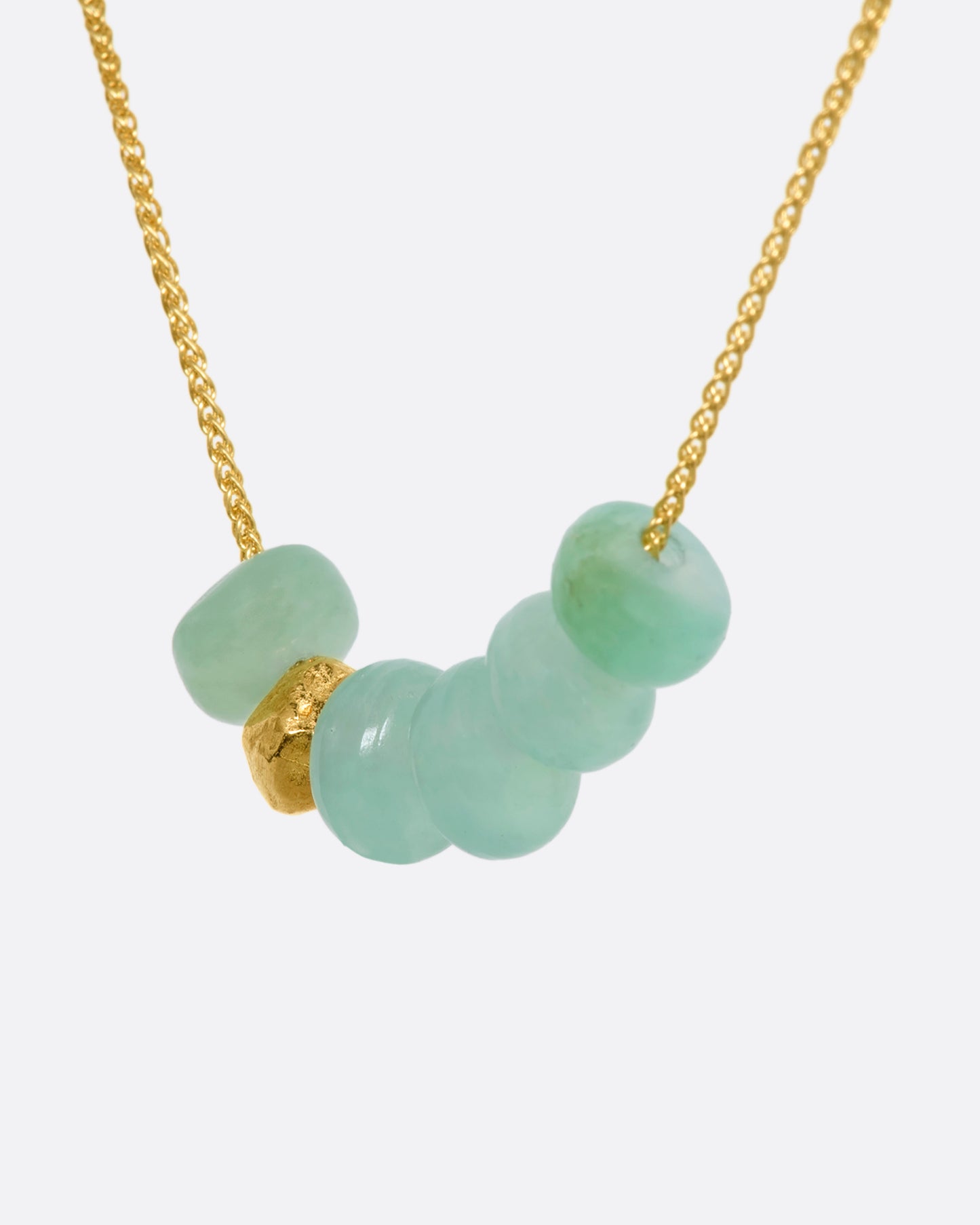 A yellow gold necklace with six beads, five of them chrysoprase and one of them textured gold. View close up from the side.