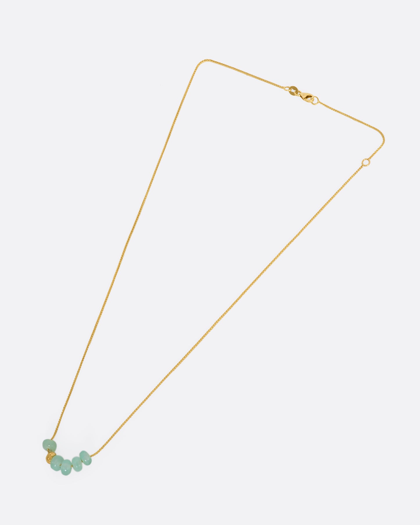 A yellow gold necklace with six beads, five of them chrysoprase and one of them textured gold. View of the entire necklace, from above.