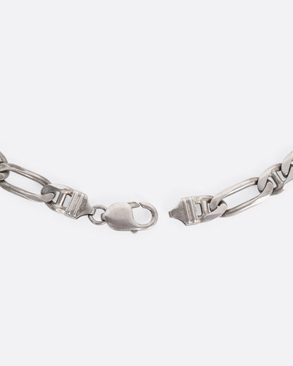A close up of the clasp on a silver figaro chain.