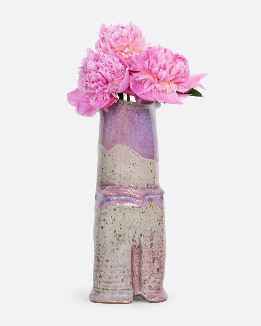 A tall ceramic vase with a tiered silhouette, fluted top, and gray and lavender color scheme. Shown from the front with pink peonies in it.
