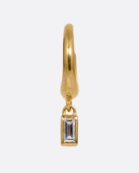 A yellow gold huggie hoop earring with a baguette diamond dangle. Shown from the front.