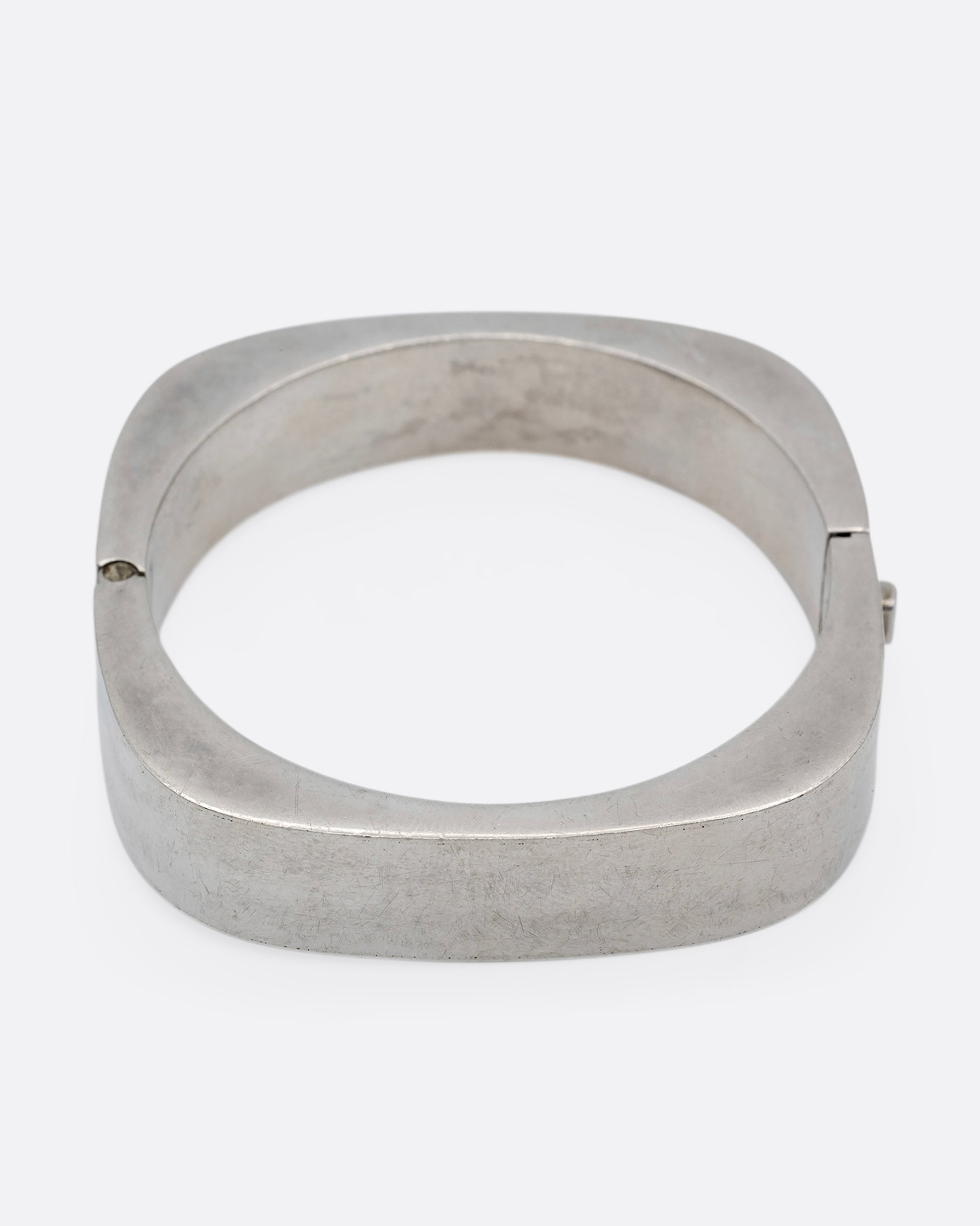 A thick square silver bracelet with a hinge and clasp. Shown from the front.