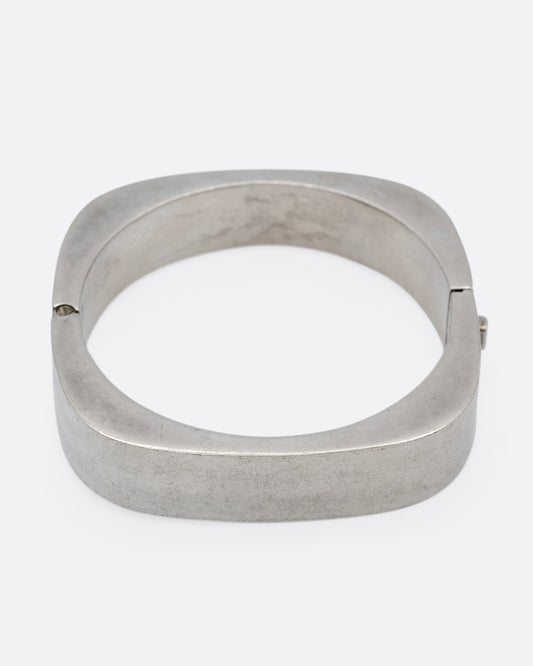 A thick square silver bracelet with a hinge and clasp. Shown from the front.