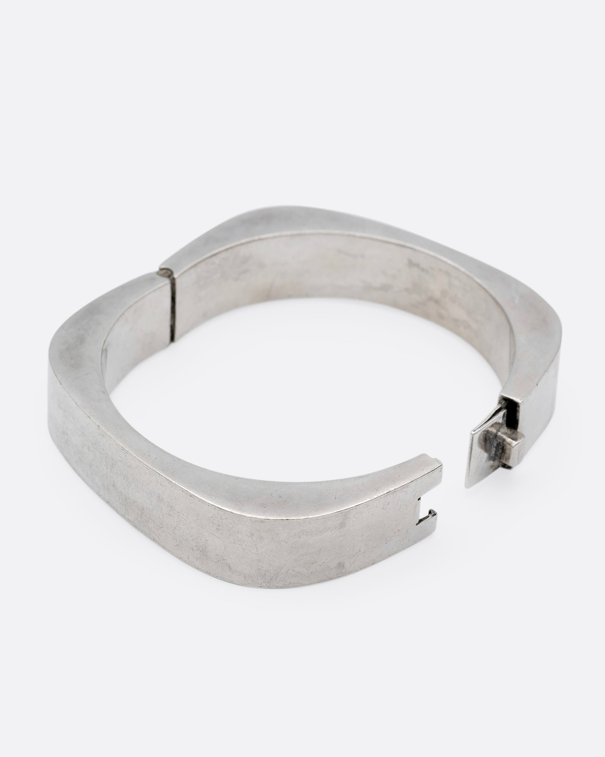 A thick square silver bracelet with a hinge and clasp. Shown open from the side.