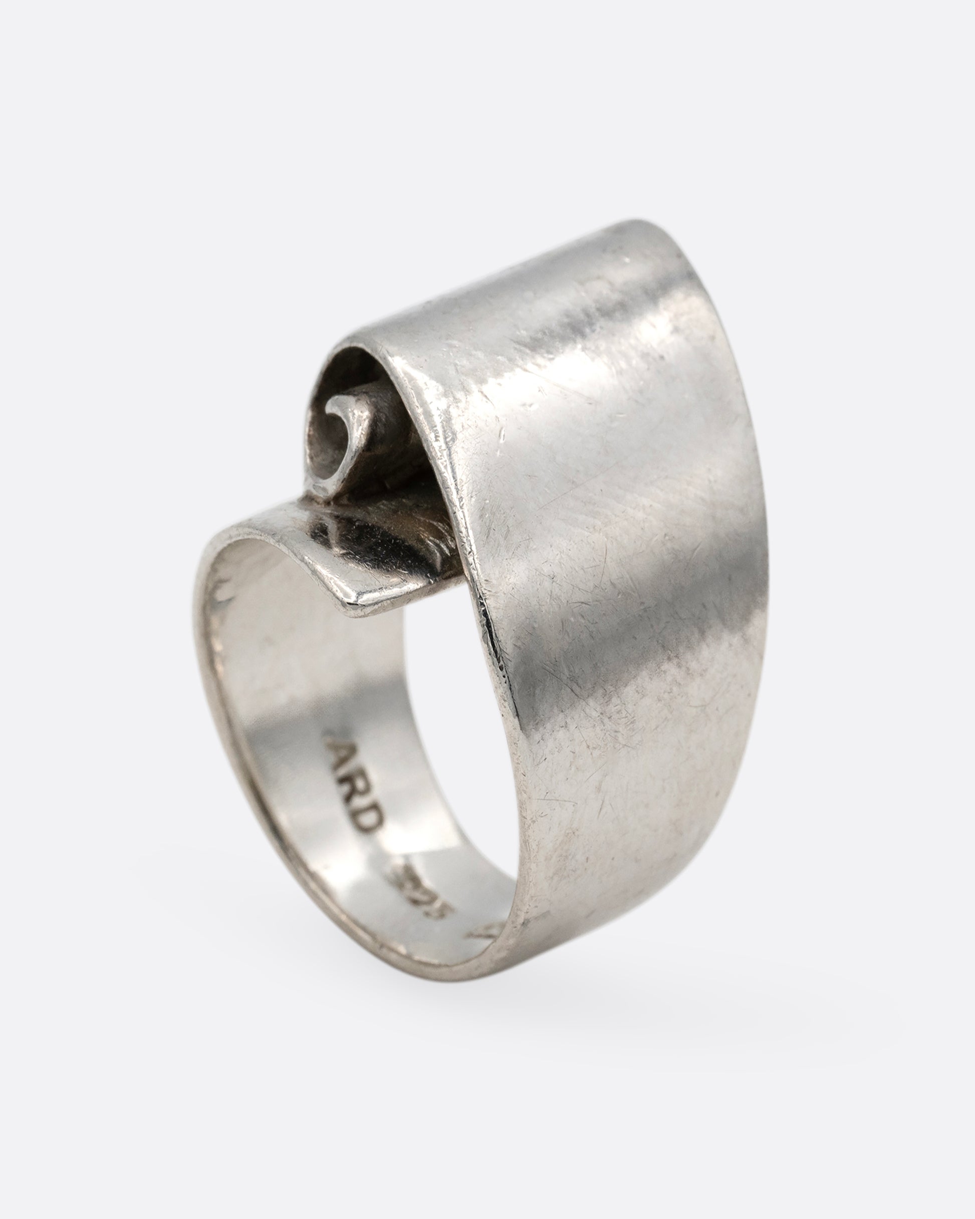 A silver ring with a scroll on its face. Shown from the bottom.