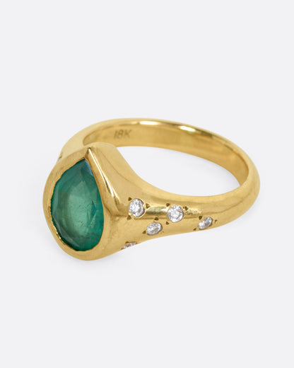 A yellow gold ring with a Zambian emerald accented by scattered diamonds, shown from the side.