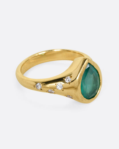 A yellow gold ring with a Zambian emerald accented by scattered diamonds, shown from the side.