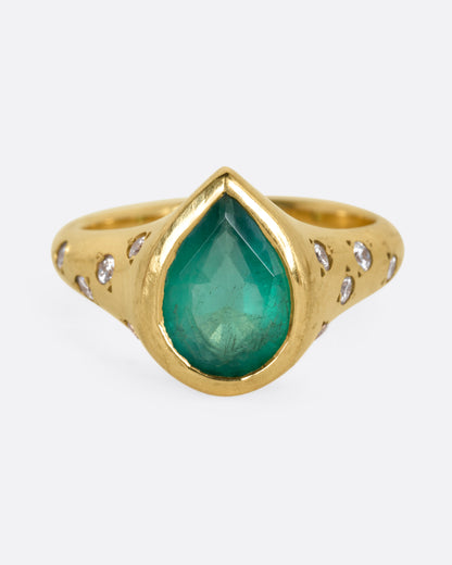 A yellow gold ring with a Zambian emerald accented by scattered diamonds, shown from the front.