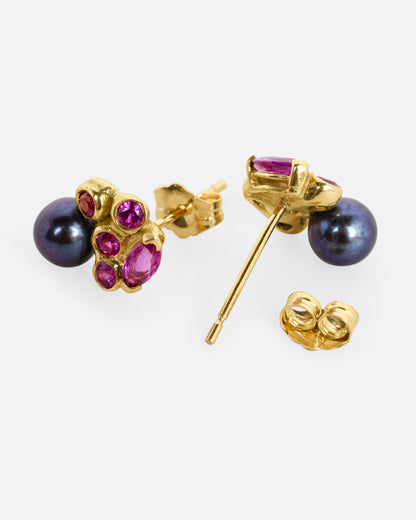 A yellow gold stud earring with rubies and a black pearl. One earring is shown from the front, the other from the back open.