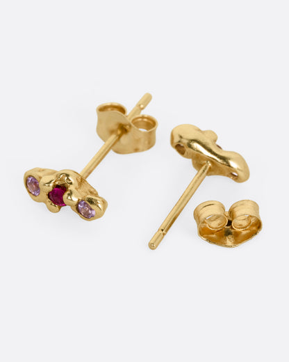 Yellow gold pink and red sapphire stud earrings, the pair laid flat showing the posts and backs