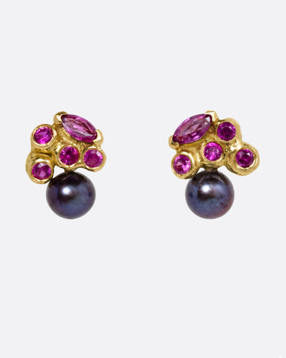 A pair of yellow gold stud earrings with rubies and black pearls. Shown from the front.