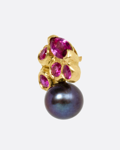 A yellow gold stud earring with rubies and a black pearl. Shown from the side.