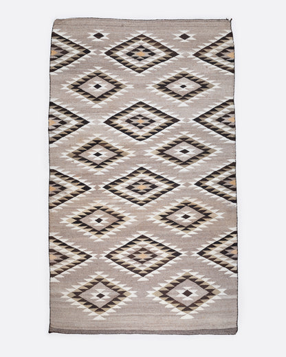 A bird's eye view of a tan, black, and white Navajo Diamond Eye Dazzler rug with a serrated diamond motif.
