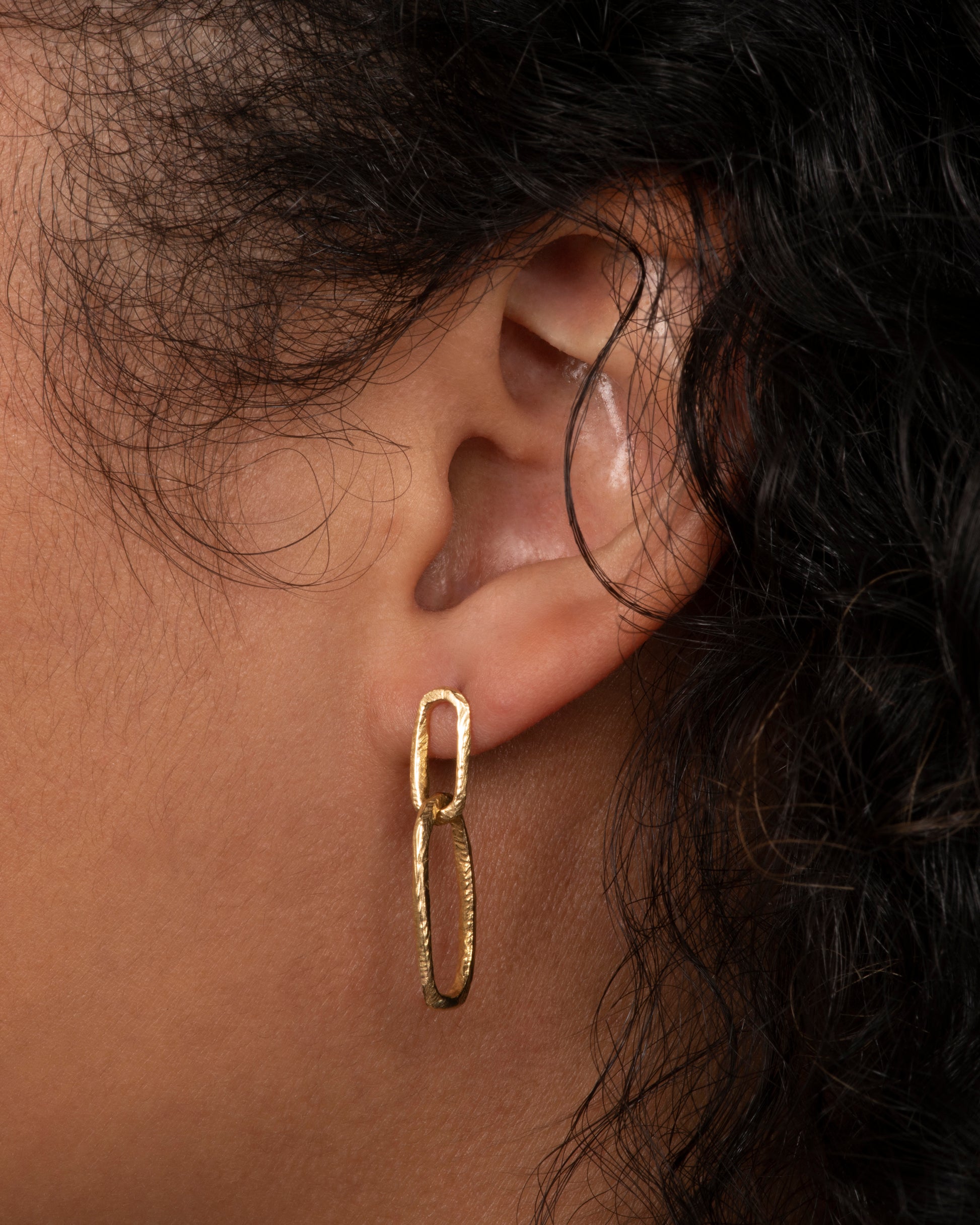 Yellow gold textured oval link earrings with stud backings. View on an ear.