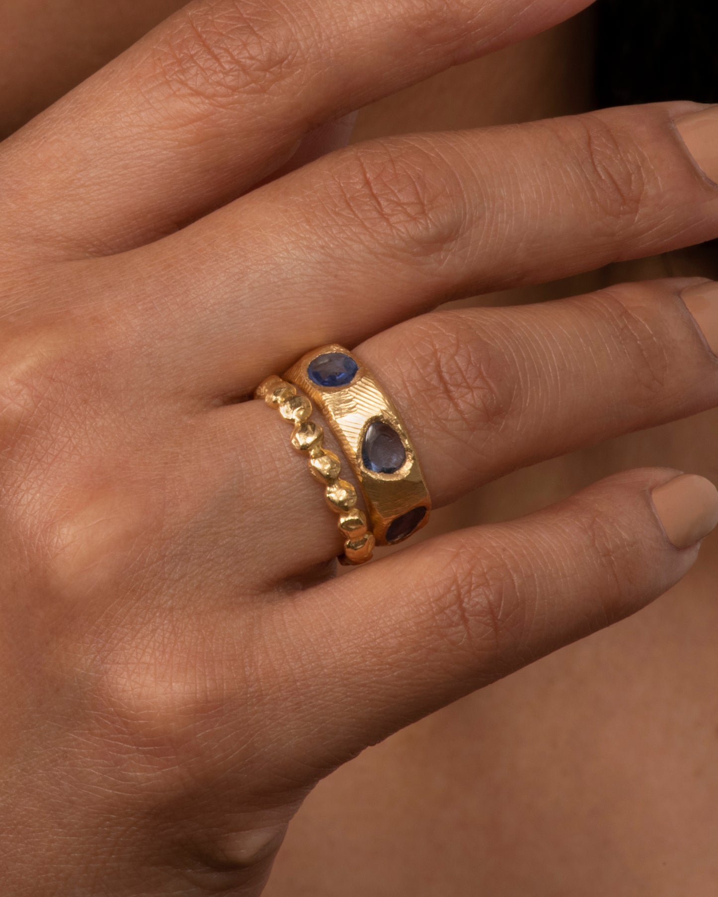 A yellow gold ring with five large blue rose cut sapphires. Shown on a hand.