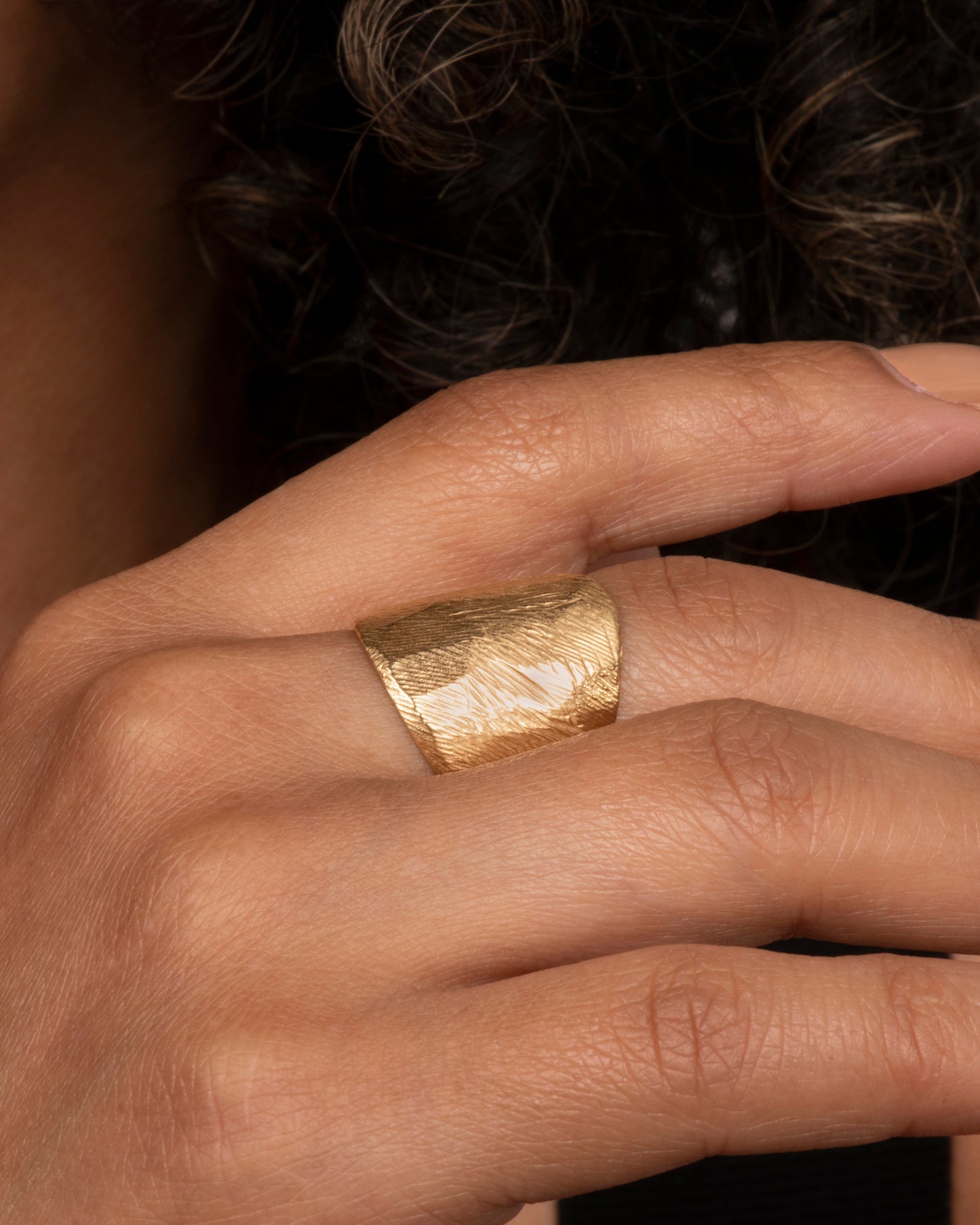 Textured yellow gold wide band ring. View on a hand.