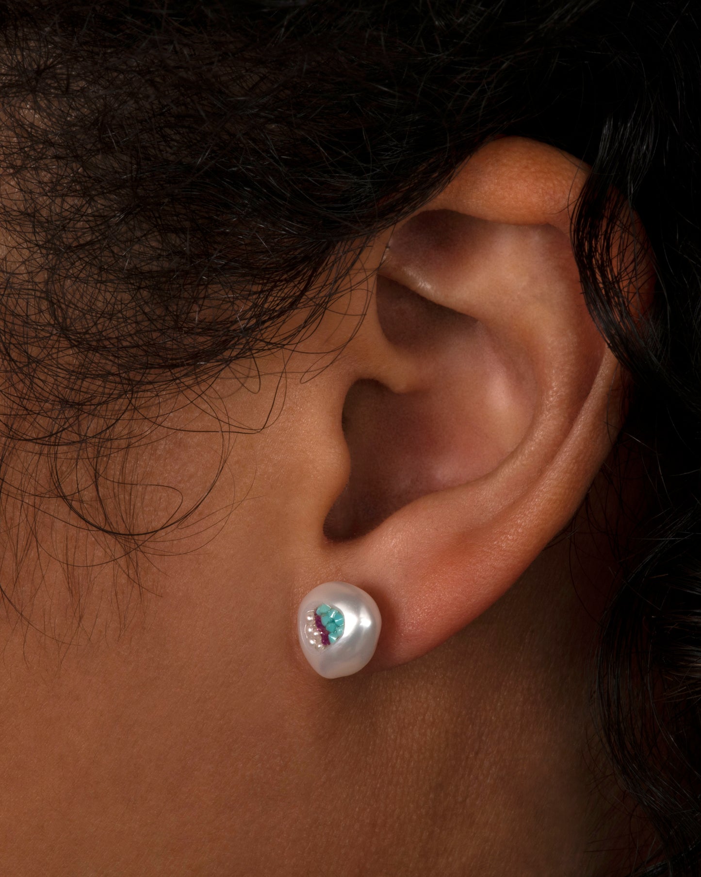 A pair of hollow pearl studs filled with seed pearls, turquoise and rubies. Shown on an ear.