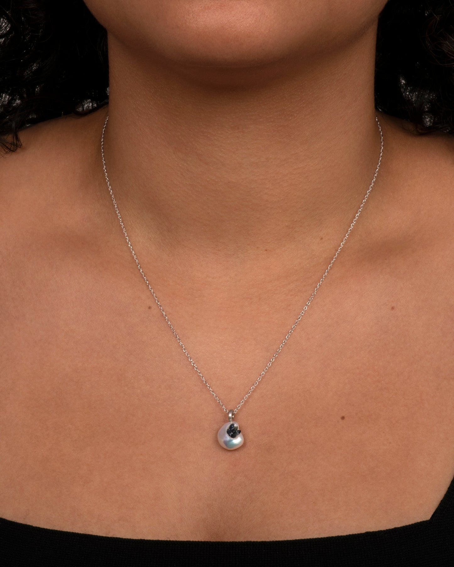 A white keshi pearl pendant filled with reclaimed sapphires hanging on a white gold chain. View on neck.