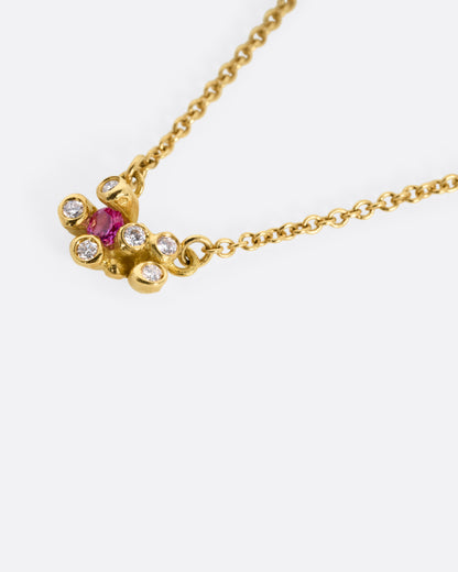 A yellow gold cable chain necklace with a pink sapphire and diamond cluster at the center, shown from the side.