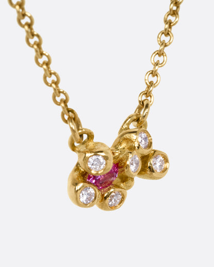 A yellow gold cable chain necklace with a pink sapphire and diamond cluster at the center, shown from the side.