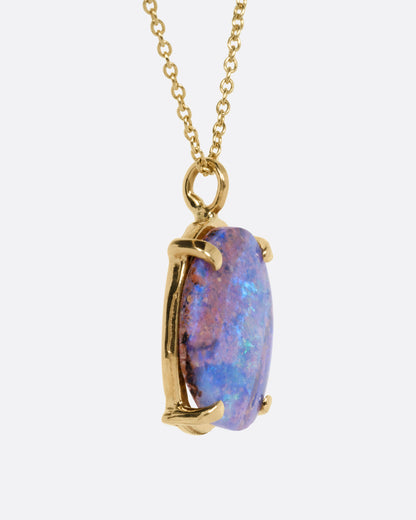 A yellow gold cable chain necklace with a prong set boulder opal pendant, shown from the side.