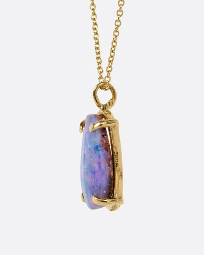A yellow gold cable chain necklace with a prong set boulder opal pendant, shown from the side.
