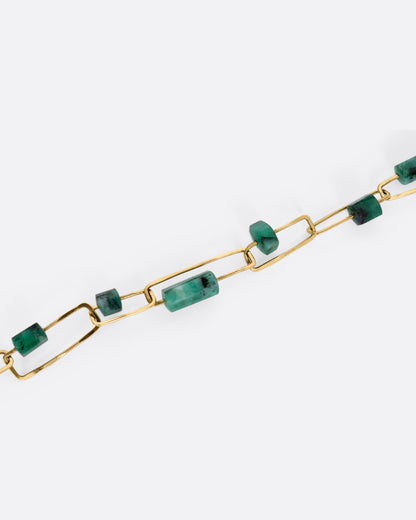 A close up of a A yellow gold paperclip chain necklace with emerald beads.