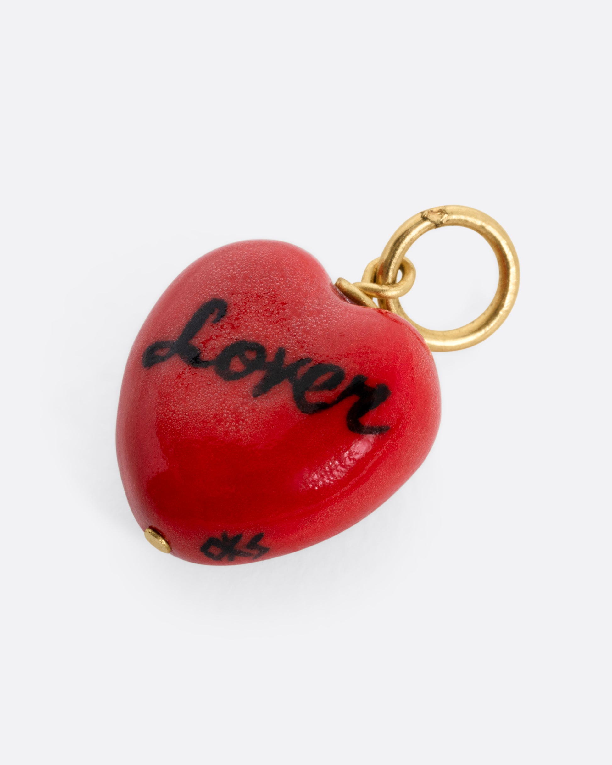 A porcelain heart charm with a face, a yellow gold bail, and 'lover' in script on the back, shown from the back.