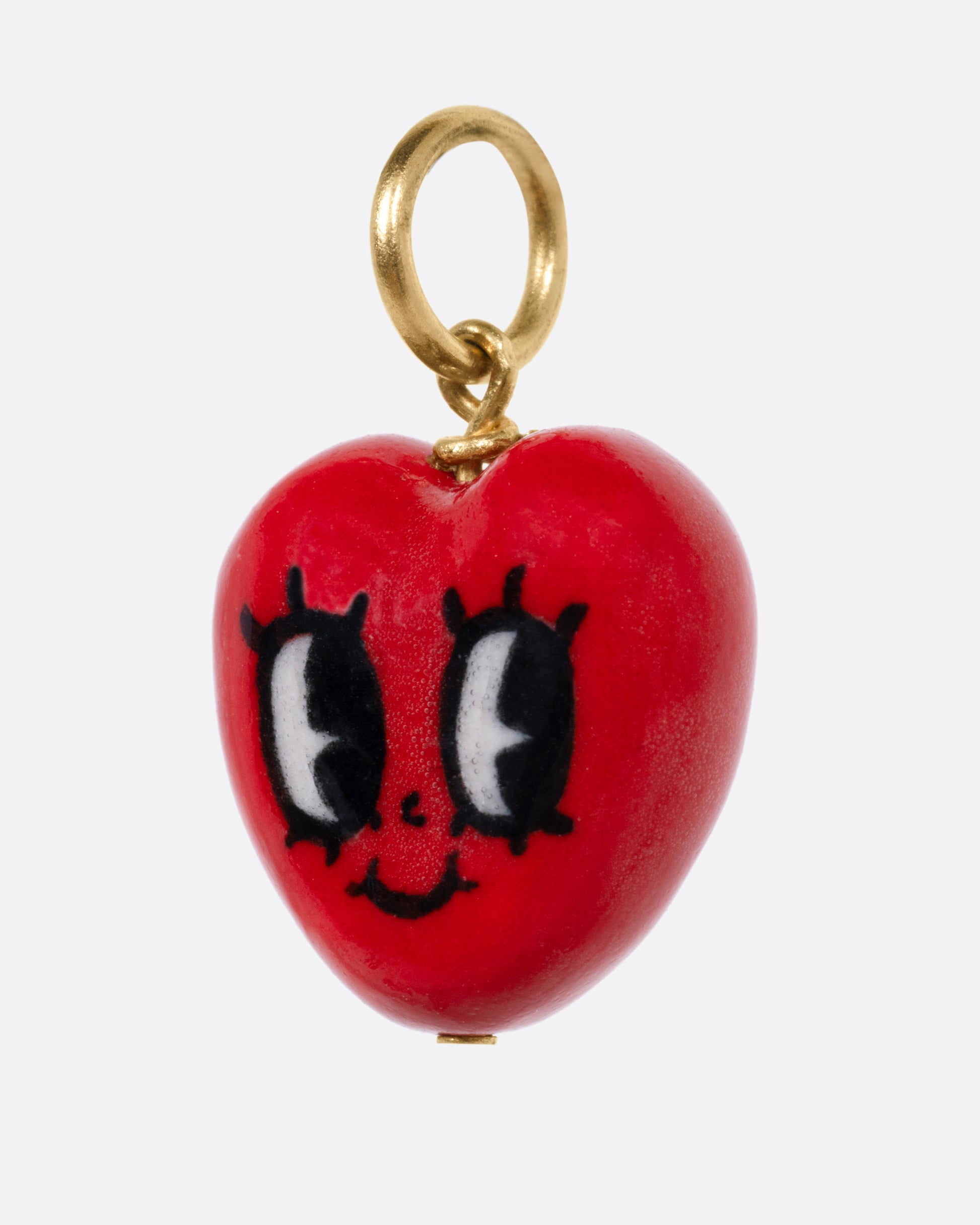 A porcelain heart charm with a face, and a yellow gold bail, shown from the side.