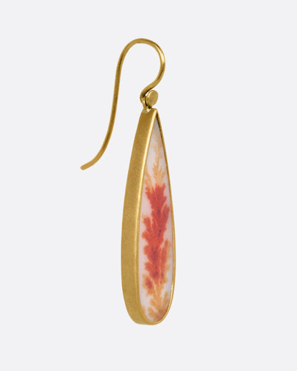 A pear shaped dendritic agate drop in a 18K gold bezel setting, shown from the side.