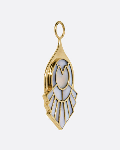 A yellow gold pendant with a feathery plumage design  inlaid with mother of pearl, shown from the side.