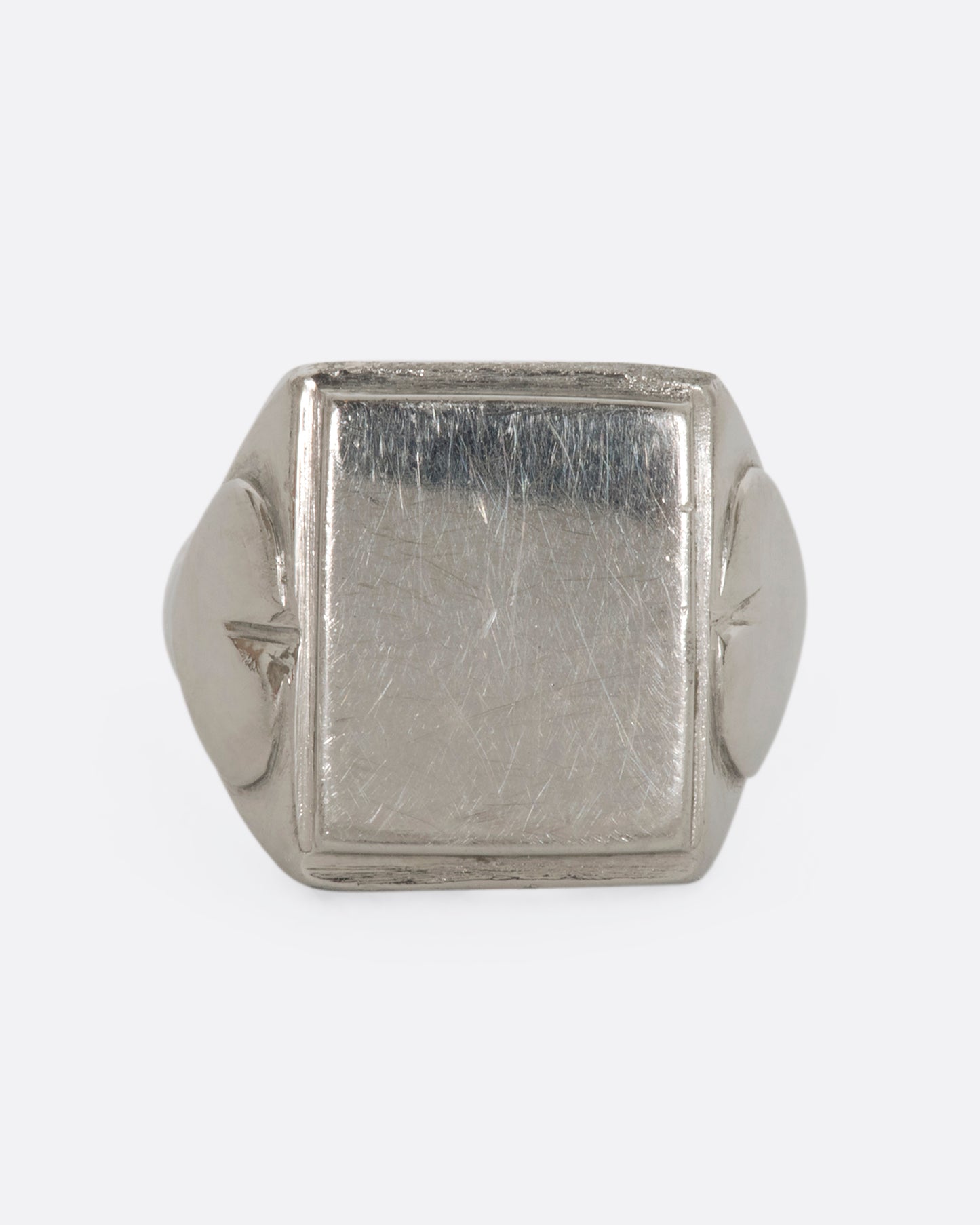 A white gold blank square signet with heart-like designs on the shoulders. View straight on from the front.