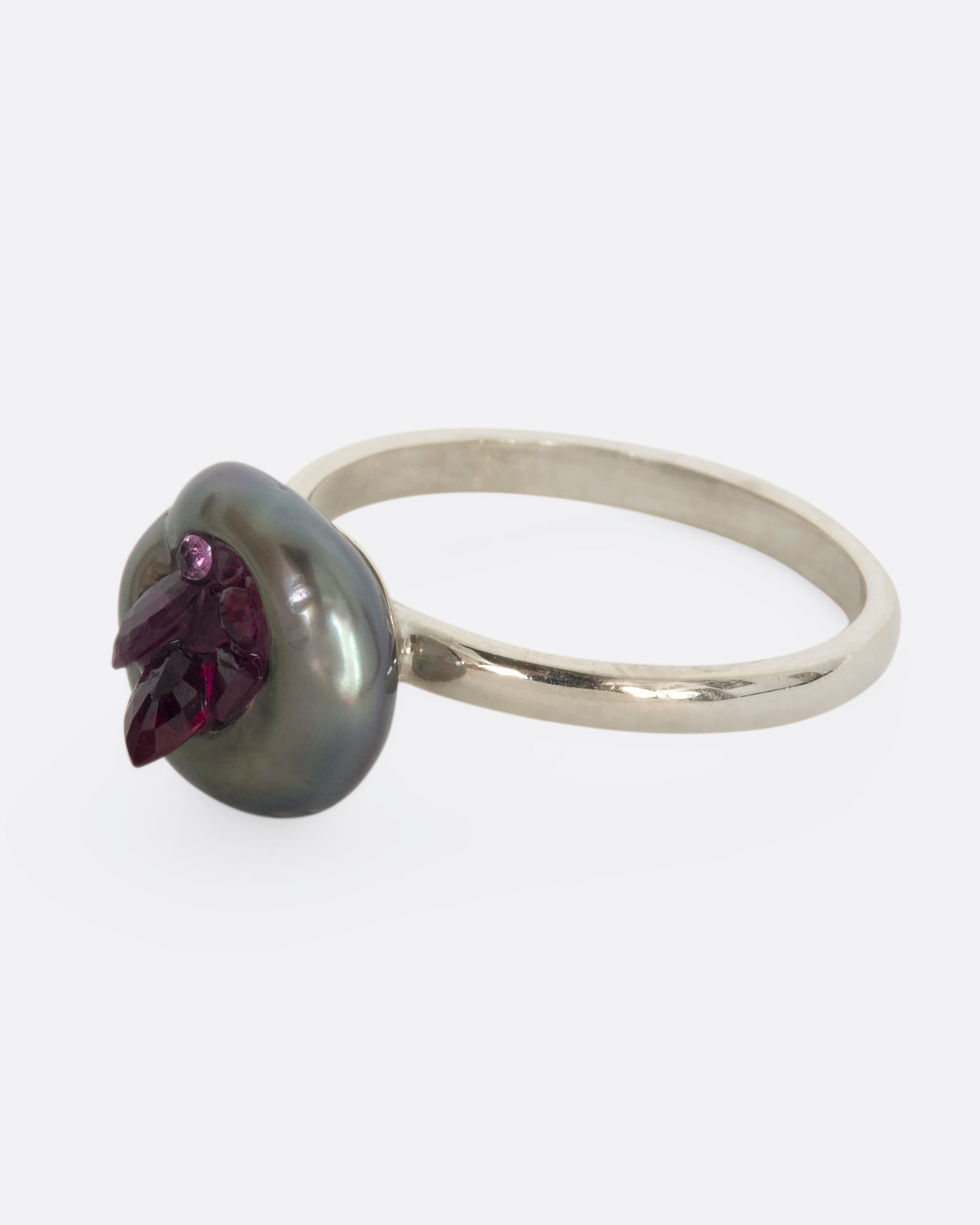 A white gold ring with carved Tahitian Keshi pearl lined with reclaimed rubies. View from the side.