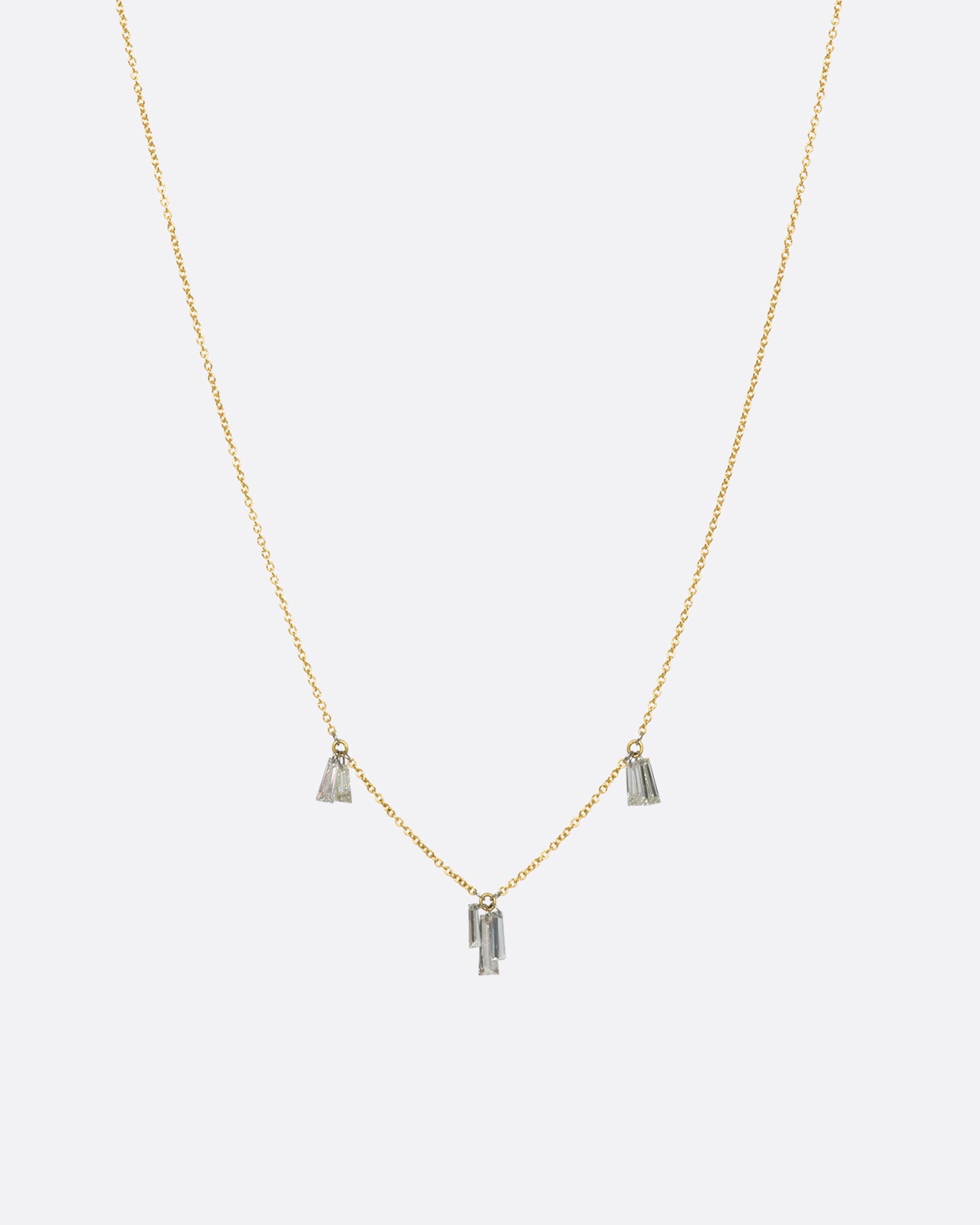 A yellow gold cable chain necklace with seven baguette diamonds dangling on platinum jump rings. View from the front.