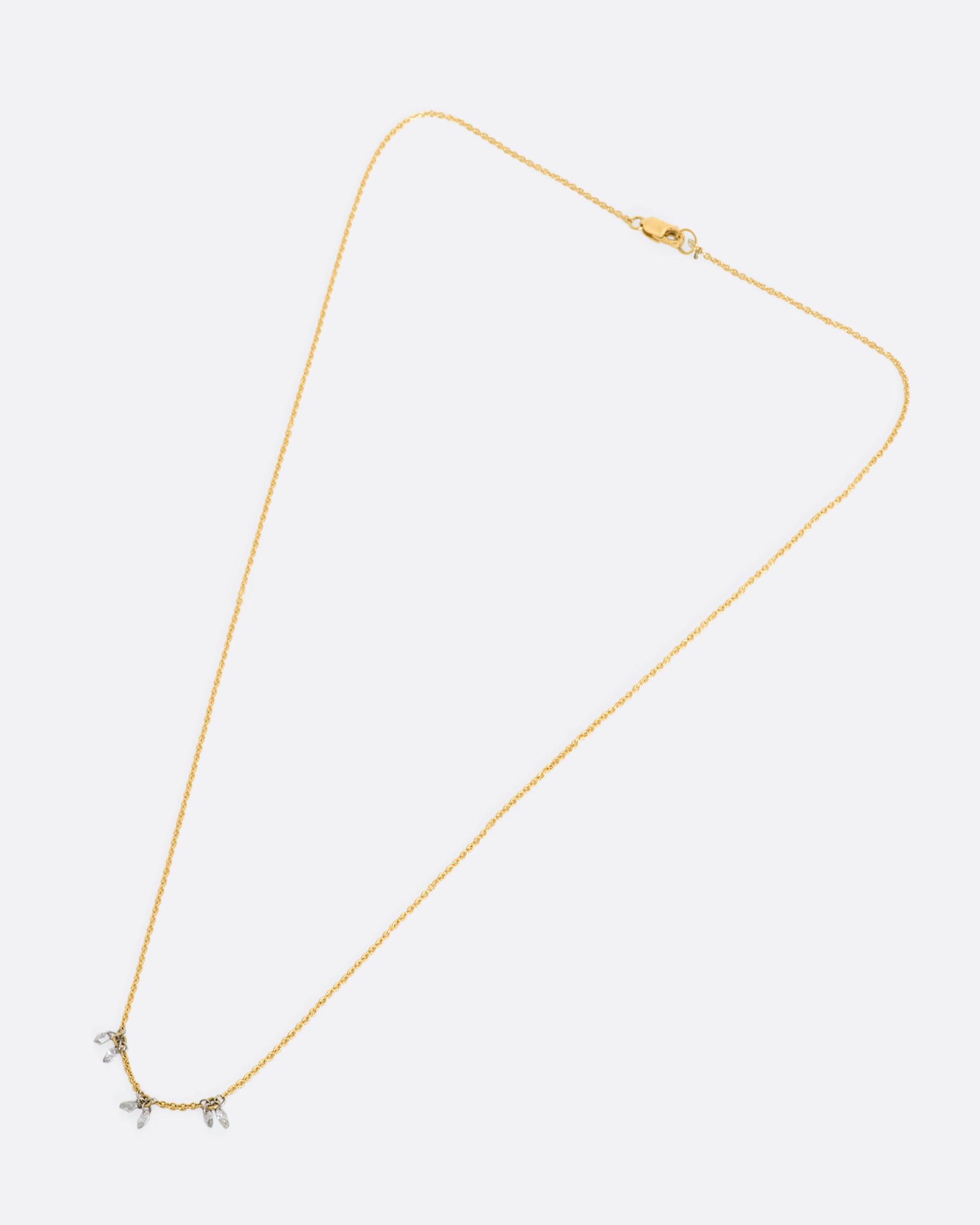 A yellow gold cable chain necklace with three stations of two marquise diamonds. View laying flat.