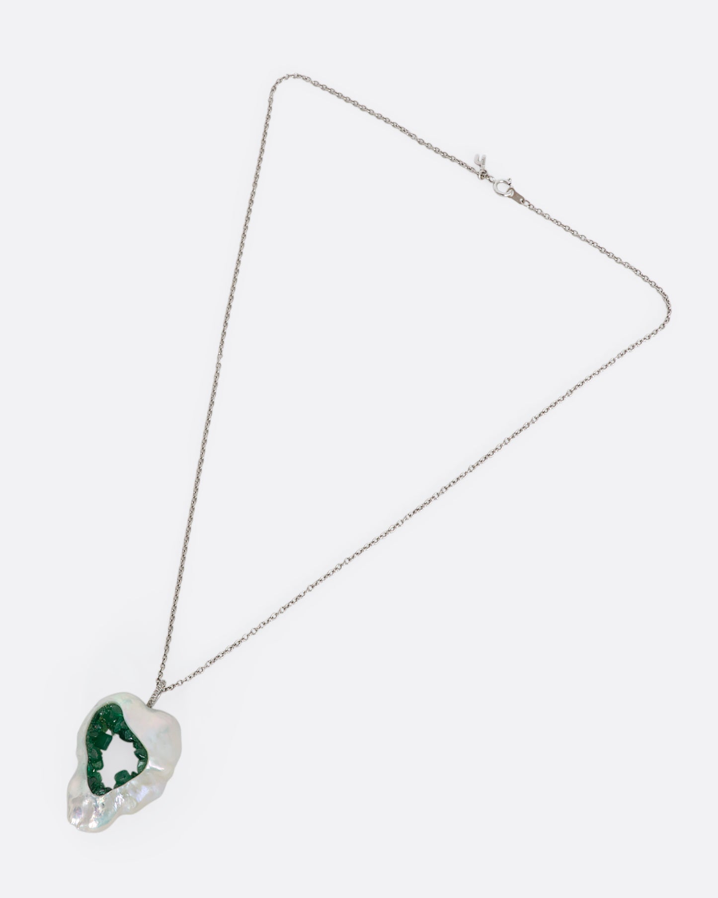 White gold necklace with a souffle pearl pendant lined in emeralds and a pave bale. View of the entire necklace laying flat.