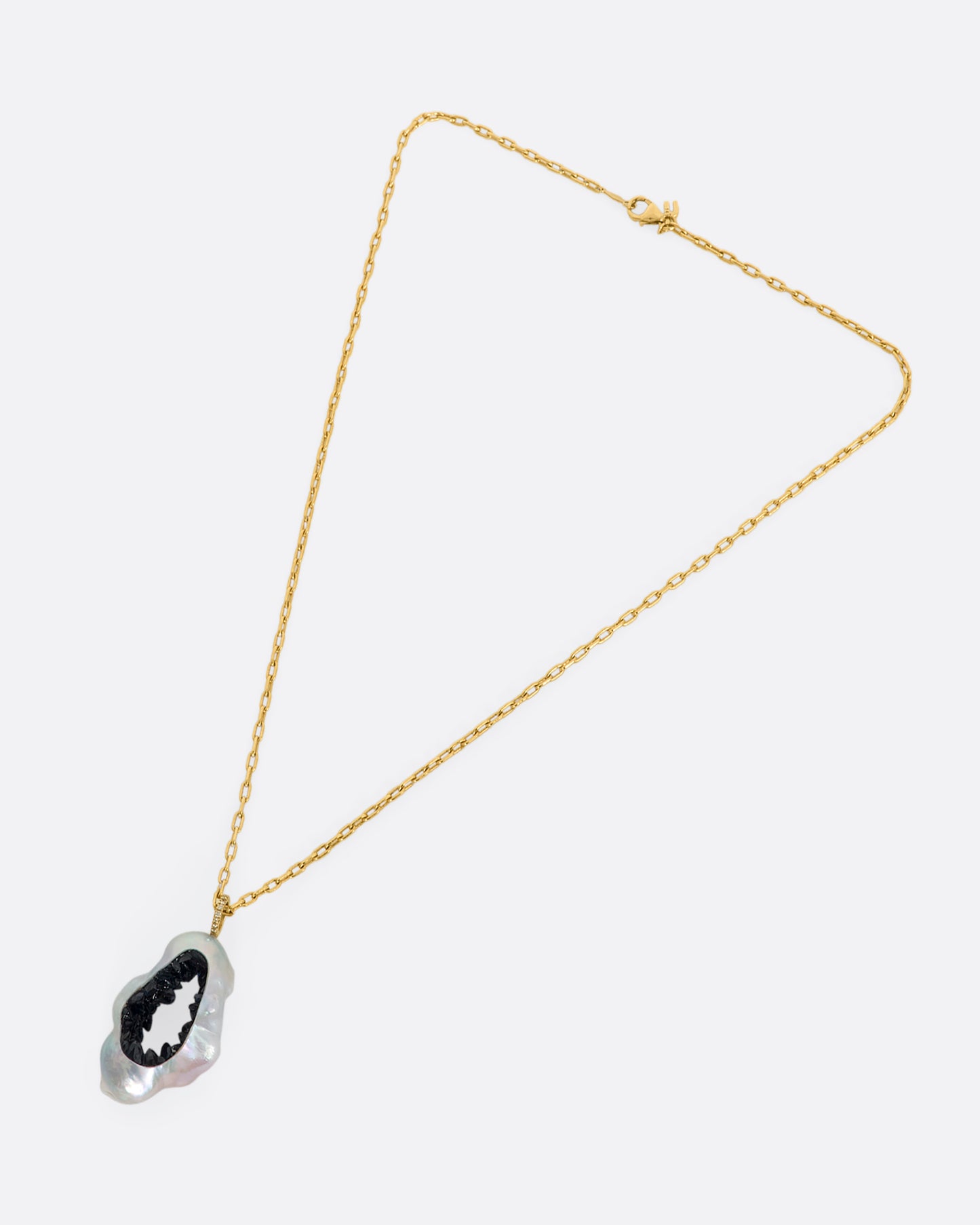 A yellow gold necklace with a hollowed souffle pearl pendant filled with a blue sapphire geode hanging from a pave diamond bale. Shown laying flat.