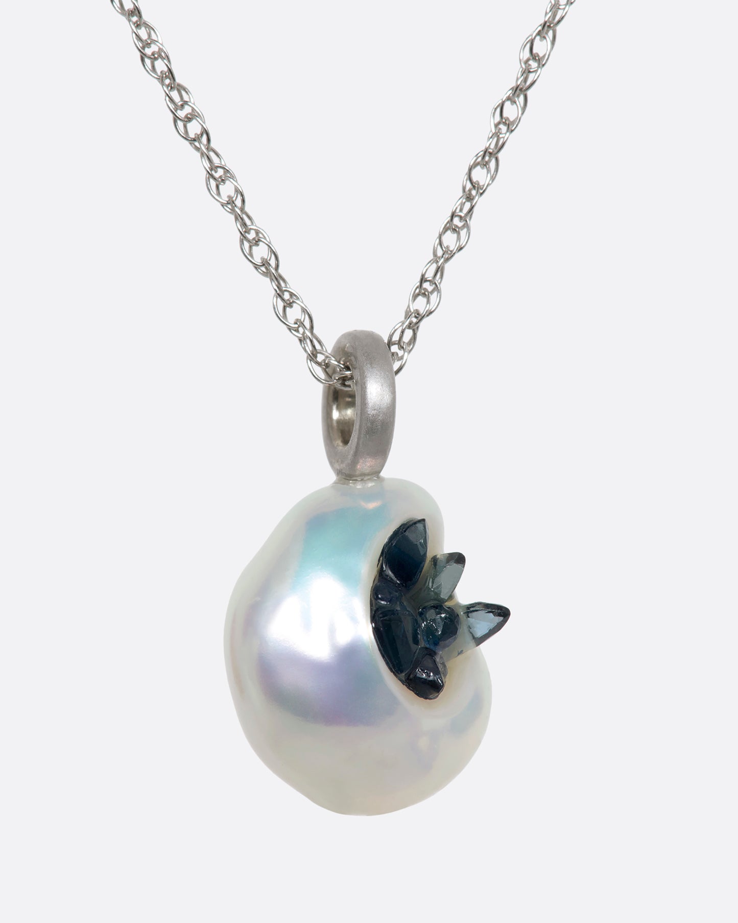 A white keshi pearl pendant filled with reclaimed sapphires hanging on a white gold chain. View from the side