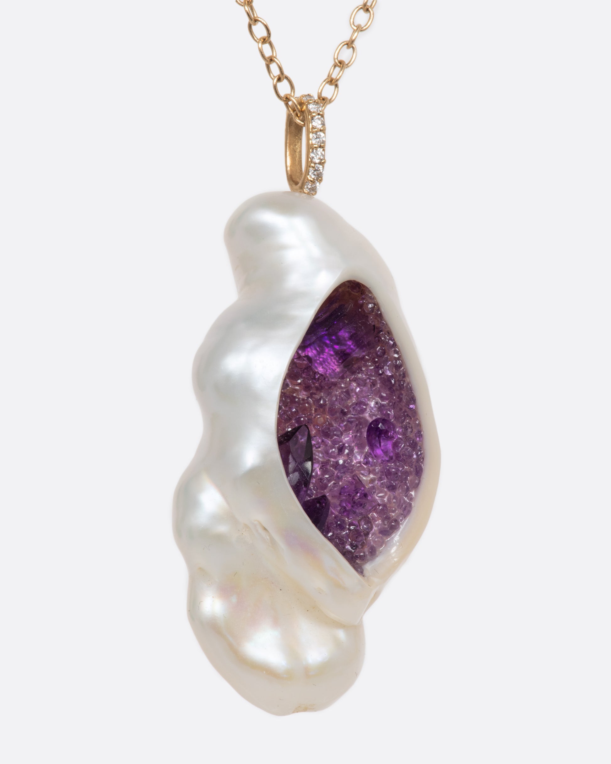 A yellow gold necklace with a hollowed out pearl pendant filled with amethysts and a pave diamond bale. Shown from the side.